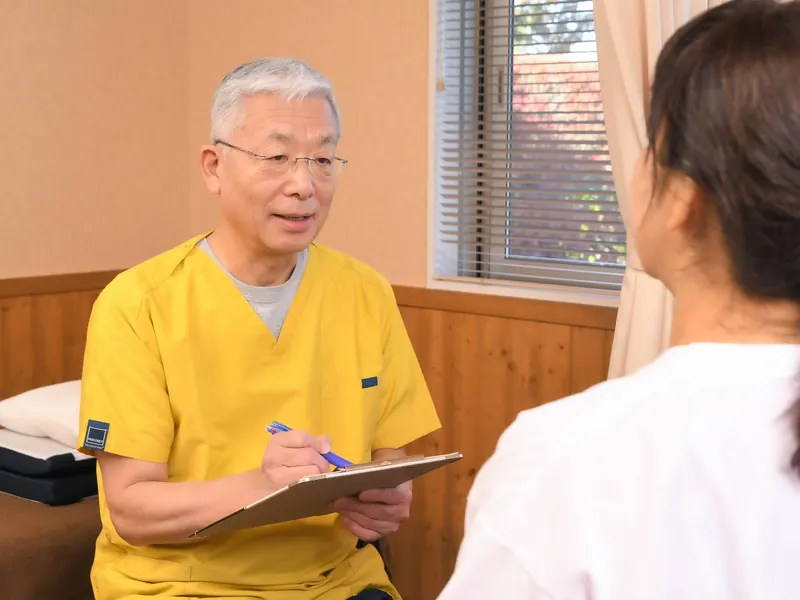 院長がうつ伏せの患者様の背中に、手のひらでやさしく触れている様子