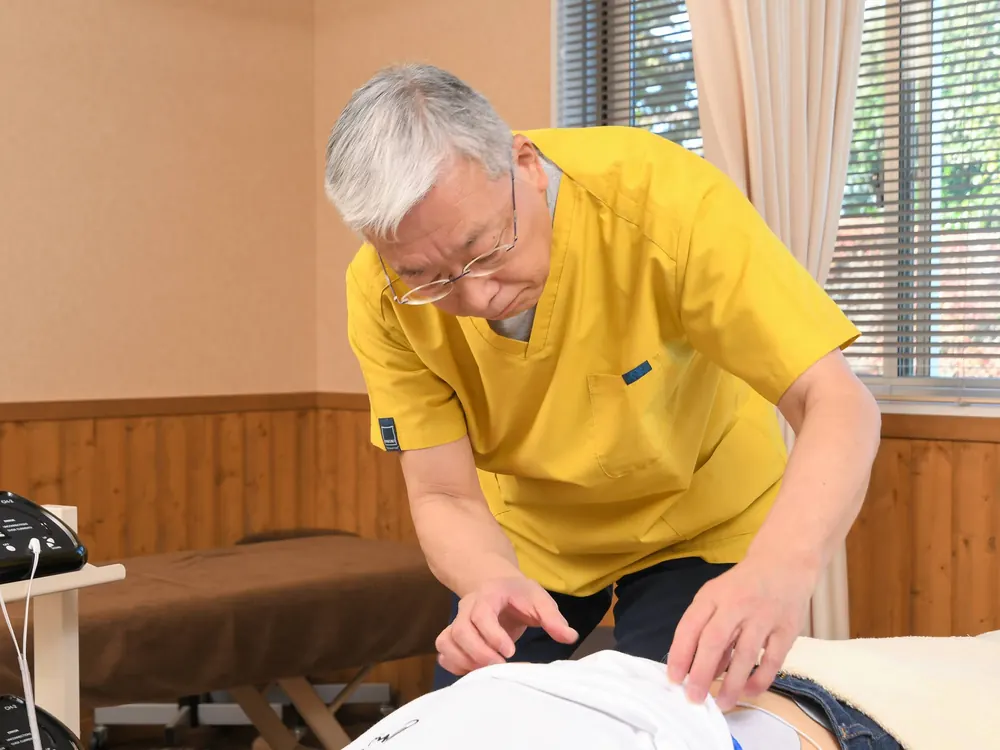 院長がうつ伏せの患者様の背中に手を当てて施術している様子