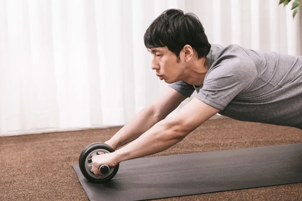 ジムでアブローラーを使って腹筋を鍛えるトレーニング中の男性