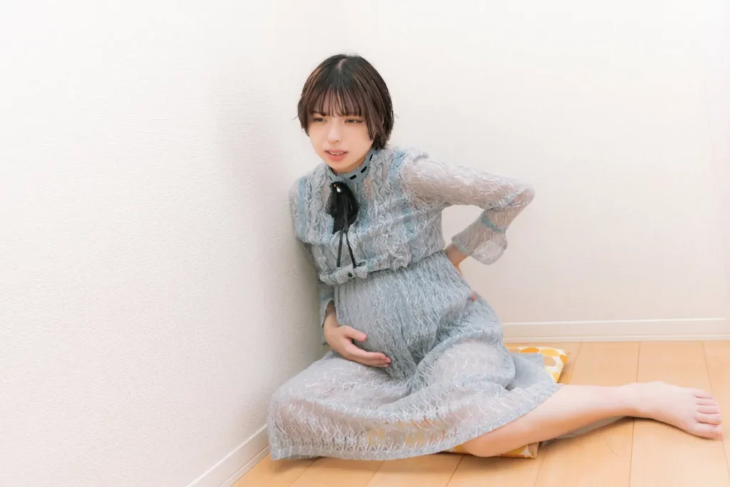 グレーのパジャマを着た妊娠後期の腰痛に悩む妊婦