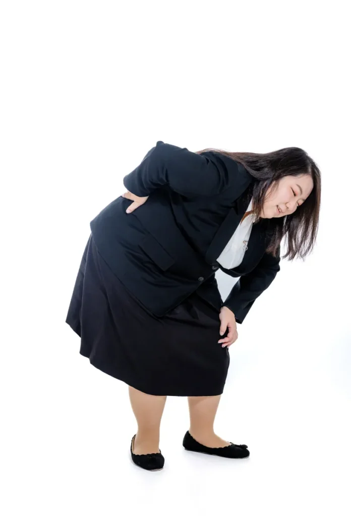 腰を痛めて身体を丸める膨よかな女性会社員のオフィスワーク